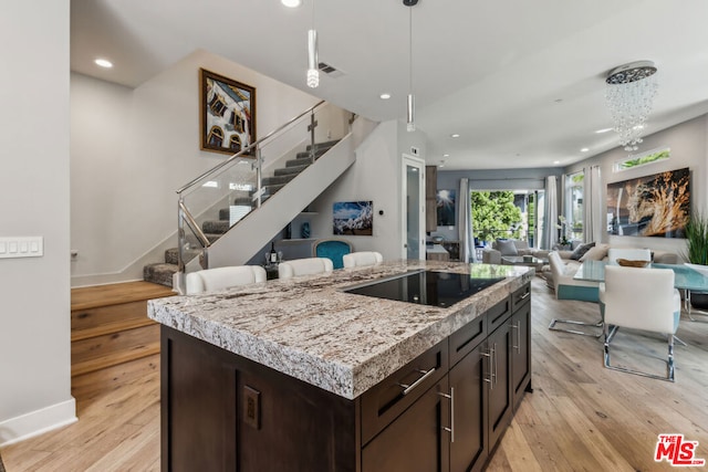 kitchen with dark brown cabinetry, a kitchen island, black electric cooktop, and light hardwood / wood-style flooring