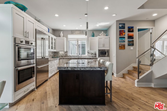 kitchen featuring a breakfast bar area, built in appliances, a kitchen island, white cabinets, and backsplash