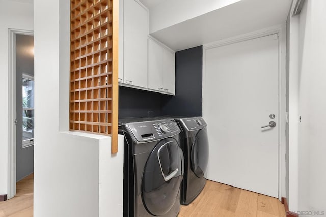 clothes washing area featuring washer and clothes dryer, light hardwood / wood-style floors, and cabinets