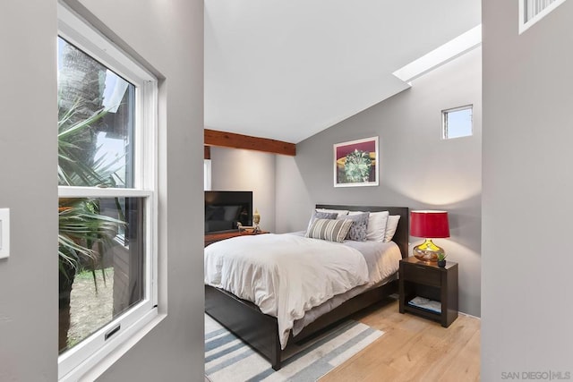 bedroom featuring multiple windows, vaulted ceiling with beams, and light hardwood / wood-style flooring