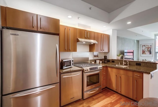 kitchen featuring sink, dark stone countertops, light hardwood / wood-style floors, kitchen peninsula, and stainless steel appliances