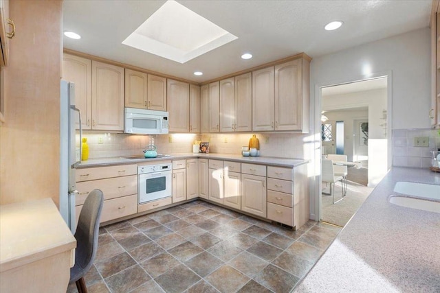 kitchen with a skylight, tasteful backsplash, sink, light brown cabinets, and white appliances