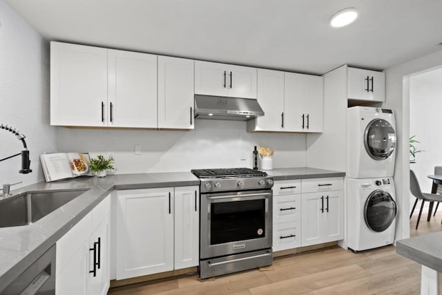 kitchen with white cabinetry, wall chimney range hood, stainless steel gas range oven, and stacked washing maching and dryer