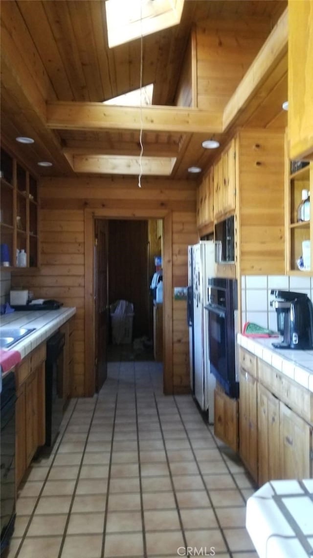 kitchen with tile countertops, black appliances, wooden walls, and light tile patterned flooring