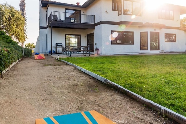 rear view of property featuring stucco siding, a lawn, fence, a balcony, and a patio area