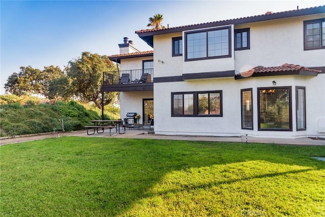 rear view of house with a patio, a balcony, a yard, a chimney, and stucco siding