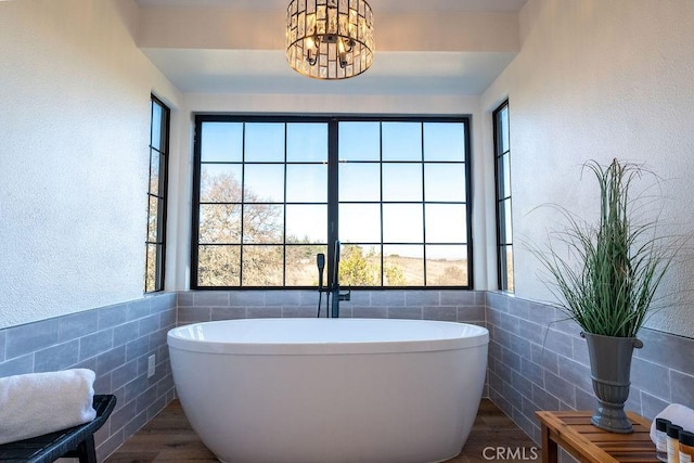 full bathroom featuring a freestanding tub, tile walls, wood finished floors, and a chandelier