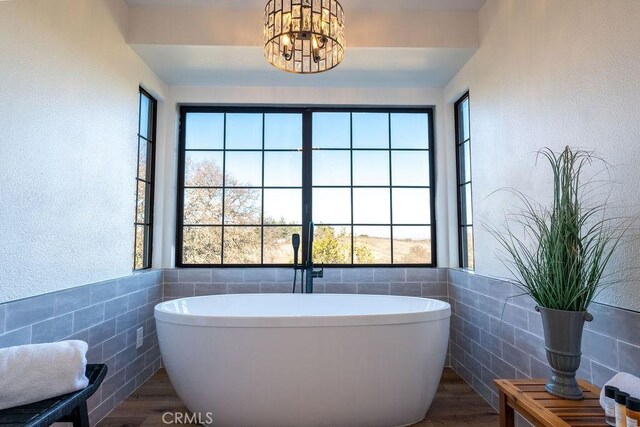 bathroom featuring an inviting chandelier, tile walls, a soaking tub, and wood finished floors