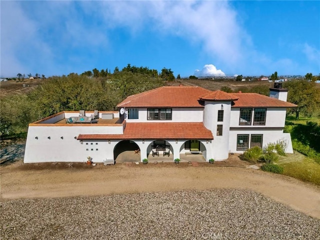 view of front of home with a tile roof, a chimney, driveway, and stucco siding