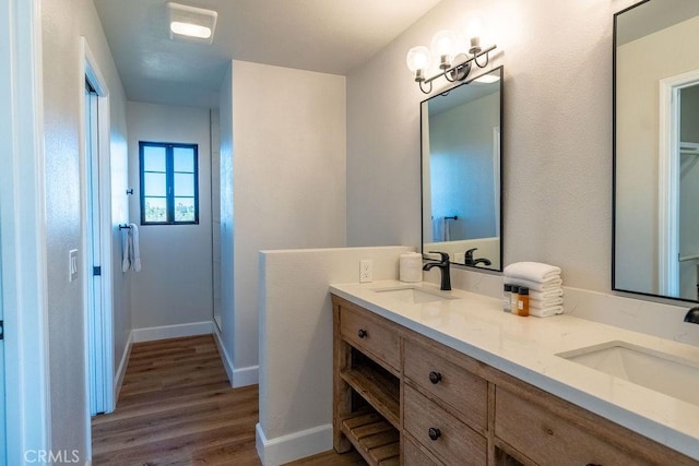 full bathroom featuring double vanity, wood finished floors, baseboards, and a sink