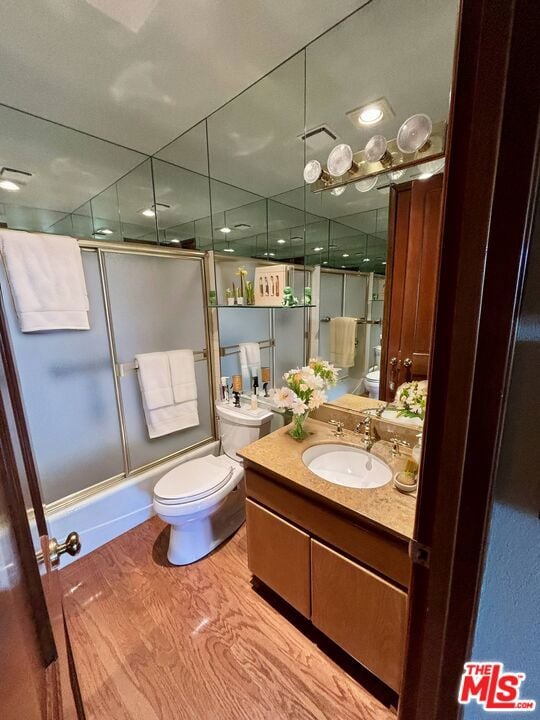 full bathroom with hardwood / wood-style flooring, vanity, toilet, and combined bath / shower with glass door