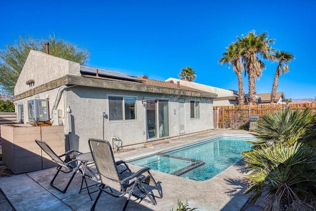 rear view of house with a swimming pool with hot tub, ac unit, a patio, and solar panels