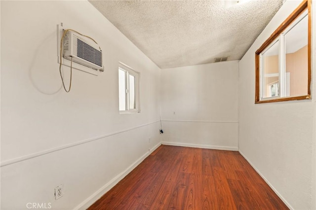 spare room featuring hardwood / wood-style floors, a wall unit AC, and a textured ceiling