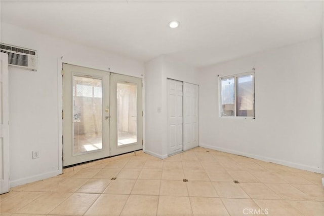 tiled spare room featuring plenty of natural light, a wall mounted air conditioner, and french doors