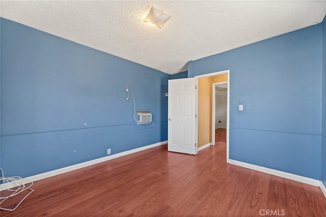 unfurnished bedroom with wood-type flooring, vaulted ceiling, an AC wall unit, and a textured ceiling