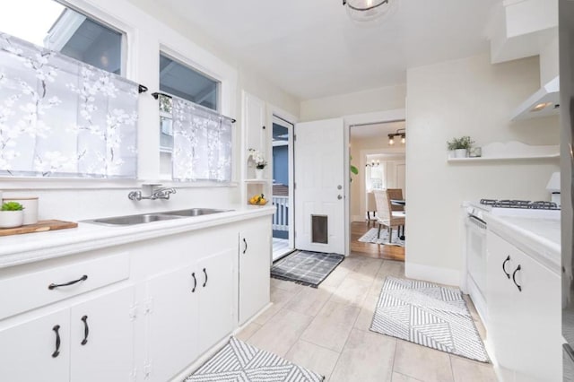 kitchen featuring sink, white range with gas stovetop, and white cabinets