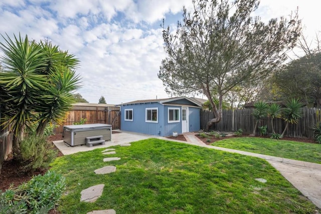 back of house with a yard, an outdoor structure, a hot tub, and a patio