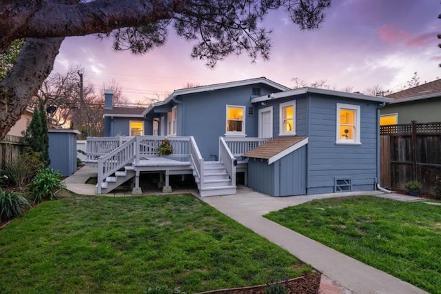 back house at dusk with a wooden deck, a lawn, and a storage unit