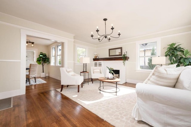 living room with wood-type flooring, a chandelier, and a brick fireplace