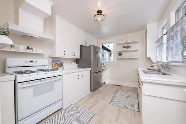 kitchen featuring wall chimney exhaust hood, sink, gas range gas stove, white cabinetry, and stainless steel refrigerator