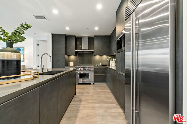 kitchen with stainless steel built in refrigerator, sink, wall oven, light wood-type flooring, and wall chimney exhaust hood