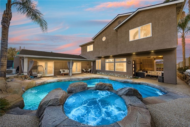 pool at dusk featuring an in ground hot tub, outdoor lounge area, and a patio area