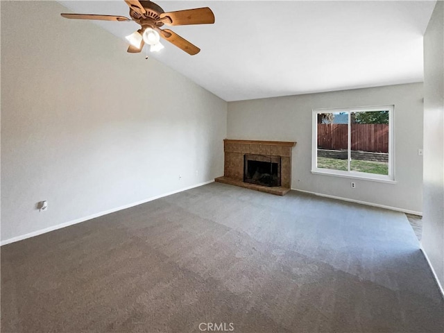 unfurnished living room with ceiling fan, a tiled fireplace, vaulted ceiling, and dark colored carpet