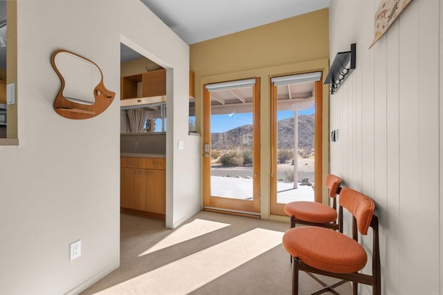 doorway with a mountain view, light colored carpet, and wood walls