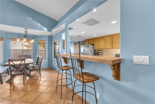 kitchen featuring pendant lighting, light tile patterned floors, a kitchen breakfast bar, tasteful backsplash, and stainless steel fridge with ice dispenser