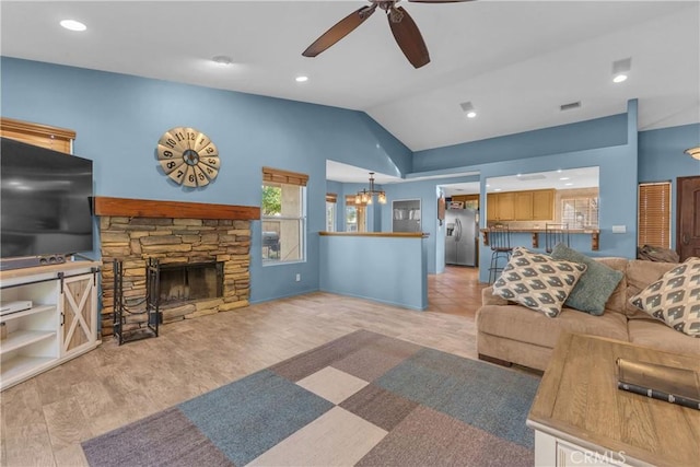 living room featuring vaulted ceiling, ceiling fan with notable chandelier, a fireplace, and light hardwood / wood-style flooring