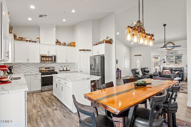 kitchen with tasteful backsplash, white cabinets, a center island, light stone counters, and stainless steel appliances