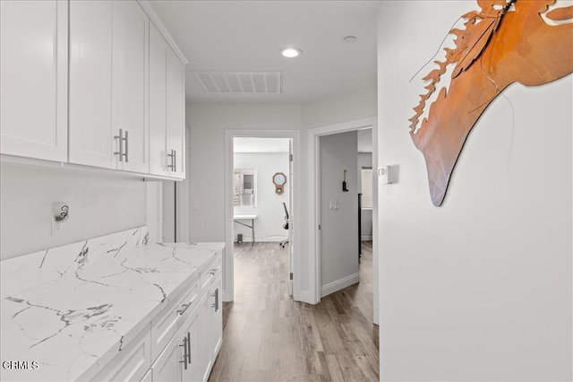 kitchen with white cabinetry, light stone counters, and light hardwood / wood-style flooring