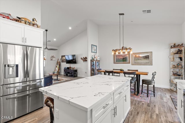 kitchen with stainless steel refrigerator with ice dispenser, white cabinetry, decorative light fixtures, and a kitchen island