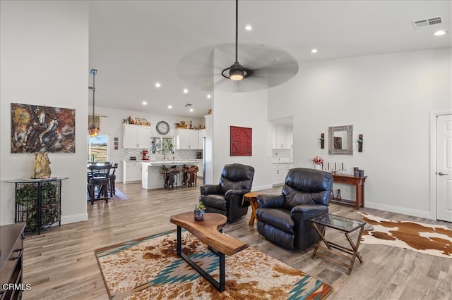 living room featuring ceiling fan, a high ceiling, and light wood-type flooring