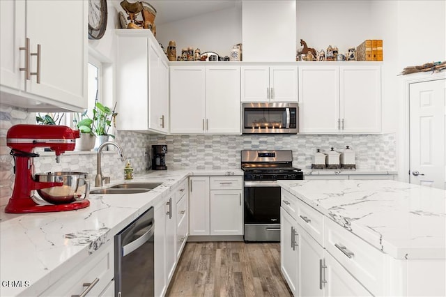 kitchen with sink, white cabinetry, light stone counters, appliances with stainless steel finishes, and backsplash