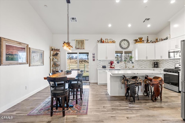 kitchen with a kitchen island, a breakfast bar, white cabinets, hanging light fixtures, and stainless steel appliances