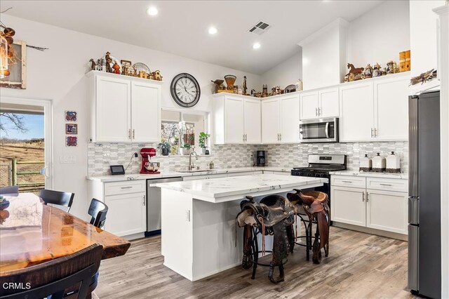 17600 Ascot Ct, Tehachapi, CA 93561 - kitchen featuring appliances with stainless steel finishes, light wood finished floors, white cabinetry, vaulted ceiling, and healthy amount of natural light