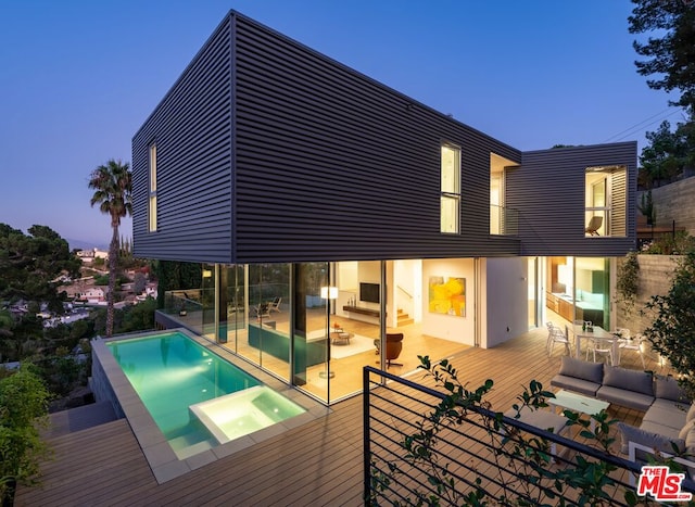 pool at dusk featuring an in ground hot tub, an outdoor living space, and a deck