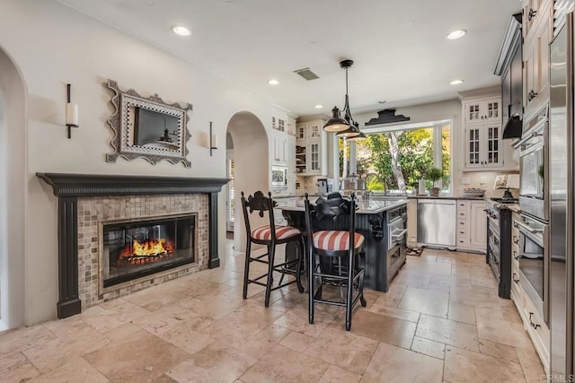 kitchen with appliances with stainless steel finishes, a breakfast bar, a fireplace, white cabinetry, and hanging light fixtures