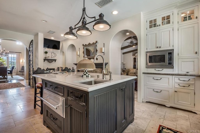 kitchen featuring stainless steel microwave, white cabinetry, decorative light fixtures, and an island with sink