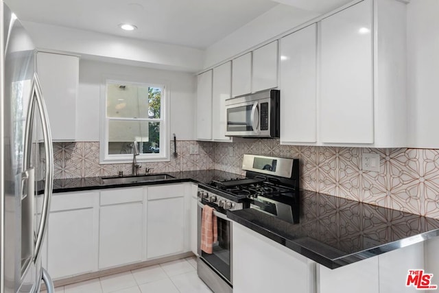 kitchen with appliances with stainless steel finishes, tasteful backsplash, white cabinetry, sink, and light tile patterned floors