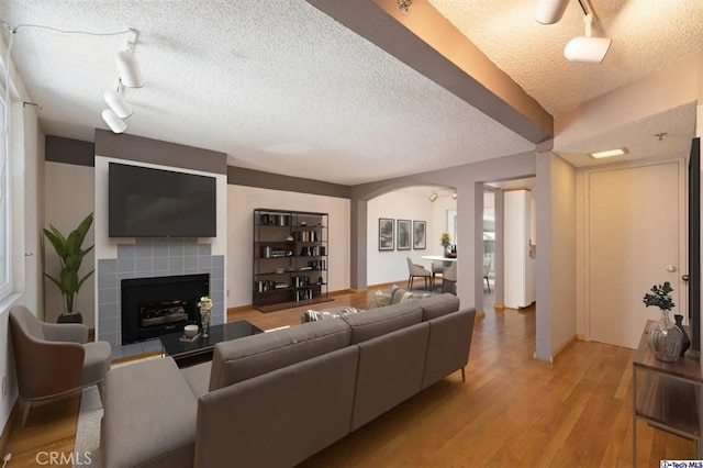 living room with light hardwood / wood-style flooring, a tile fireplace, a textured ceiling, and track lighting