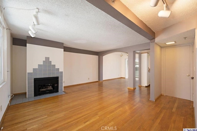 unfurnished living room with track lighting, a tiled fireplace, light hardwood / wood-style flooring, and a textured ceiling