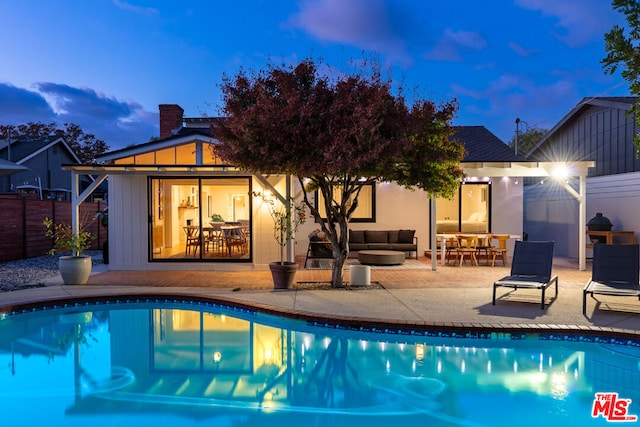 pool at dusk with outdoor lounge area and a patio