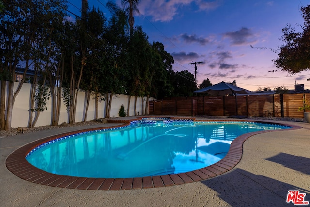 pool at dusk featuring a patio