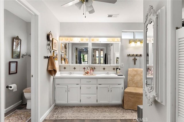 bathroom with toilet, vanity, hardwood / wood-style flooring, ceiling fan, and decorative backsplash