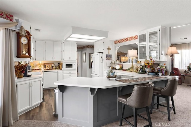 kitchen featuring a kitchen breakfast bar, dark colored carpet, white cabinets, and white appliances