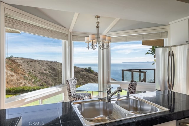 kitchen featuring stainless steel refrigerator, sink, white cabinets, hanging light fixtures, and a water view