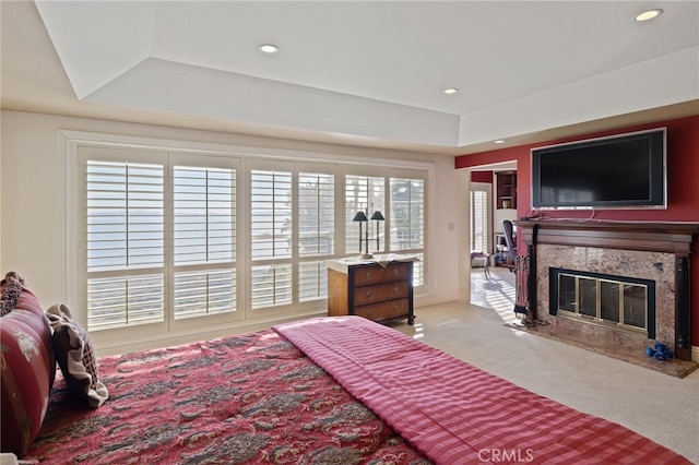 carpeted bedroom featuring a tray ceiling and a premium fireplace