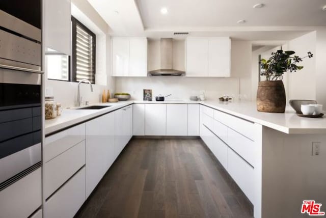 kitchen with wall chimney exhaust hood, sink, dark hardwood / wood-style floors, oven, and white cabinets